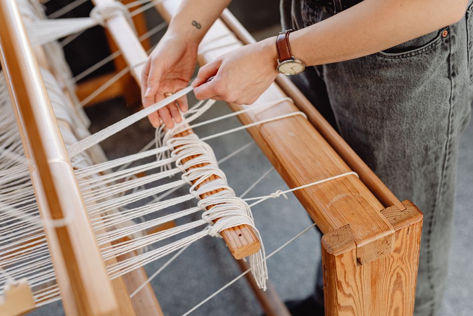 Hands weaving a rug on a wooden loom with wool threads, showcasing traditional crafting techniques.