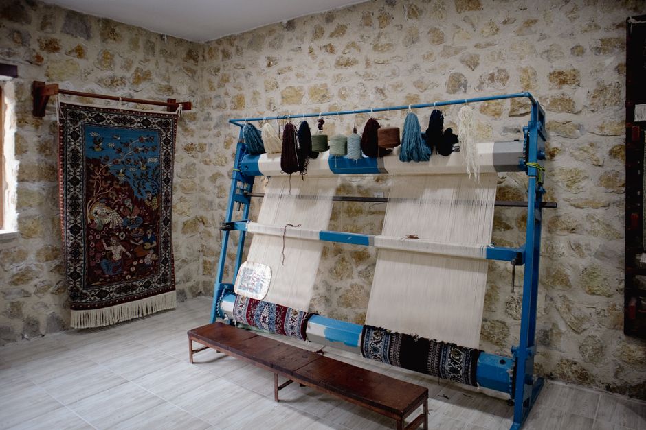 A traditional loom with colorful threads in a rustic stone-walled room.