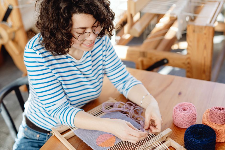 A woman enthusiastically weaving yarn on a wooden loom, showcasing handmade craft.
